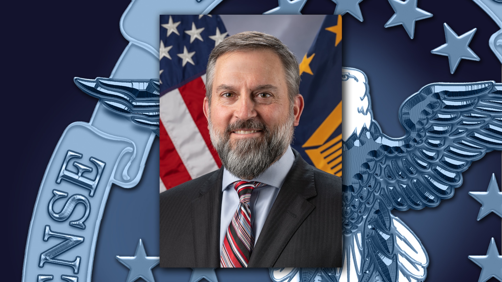 Close up of a man in a suit sitting in front of flags