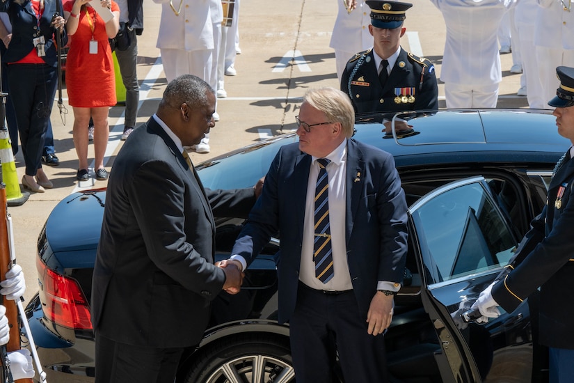 After one man emerges from a car, another man welcomes him with a handshake.