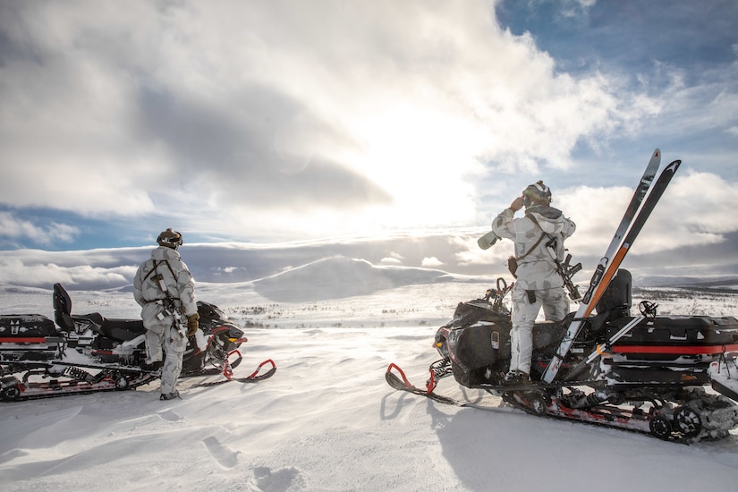 Two service members ride snowmobiles.