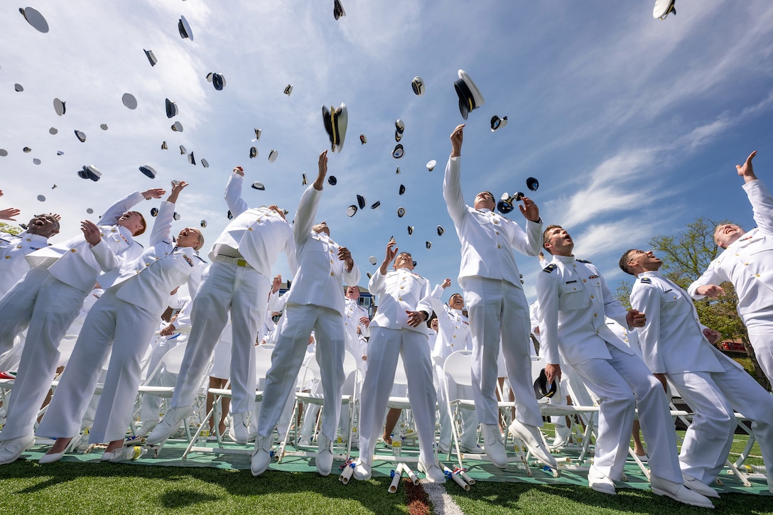Coast Guardsmen toss their covers in the air while standing on a field.
