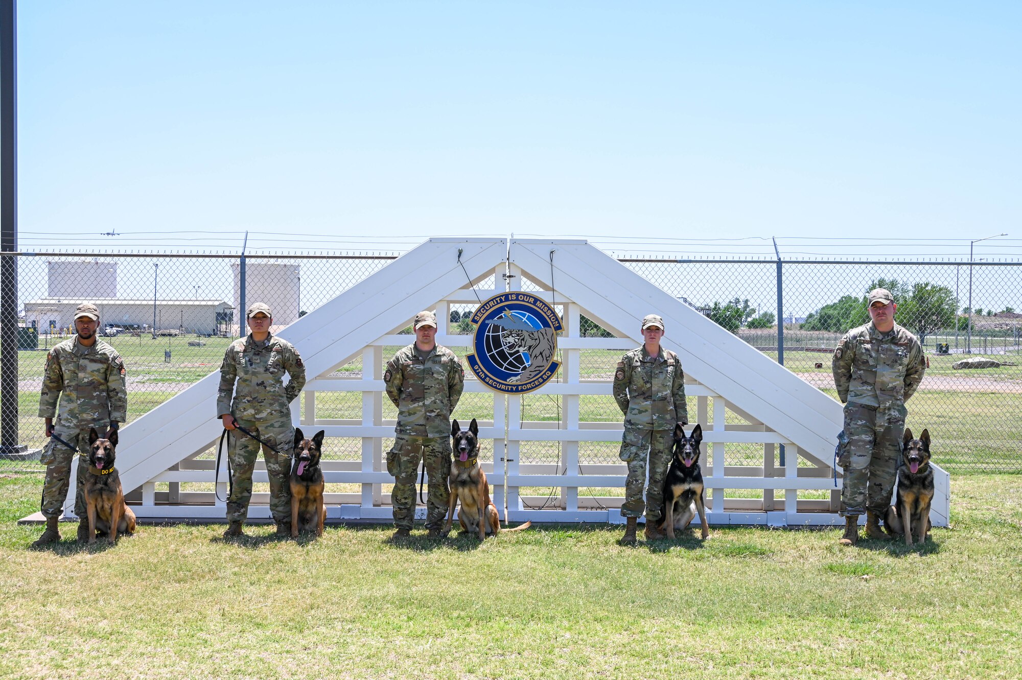 five security forces members stand with their dogs by their side