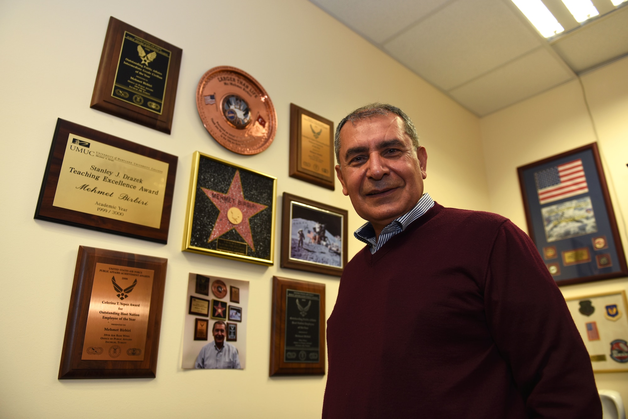 Mehmet Birbiri, 39th Air Base Wing Public Affairs host nation advisor, poses for a photo in his office at Incirlik Air Base, Turkey, 22 March 2021. Birbiri stands in front of several awards and recognitions he’s received over his many years of service. (U.S Air Force Photo by Senior Airman Matthew Angulo)
