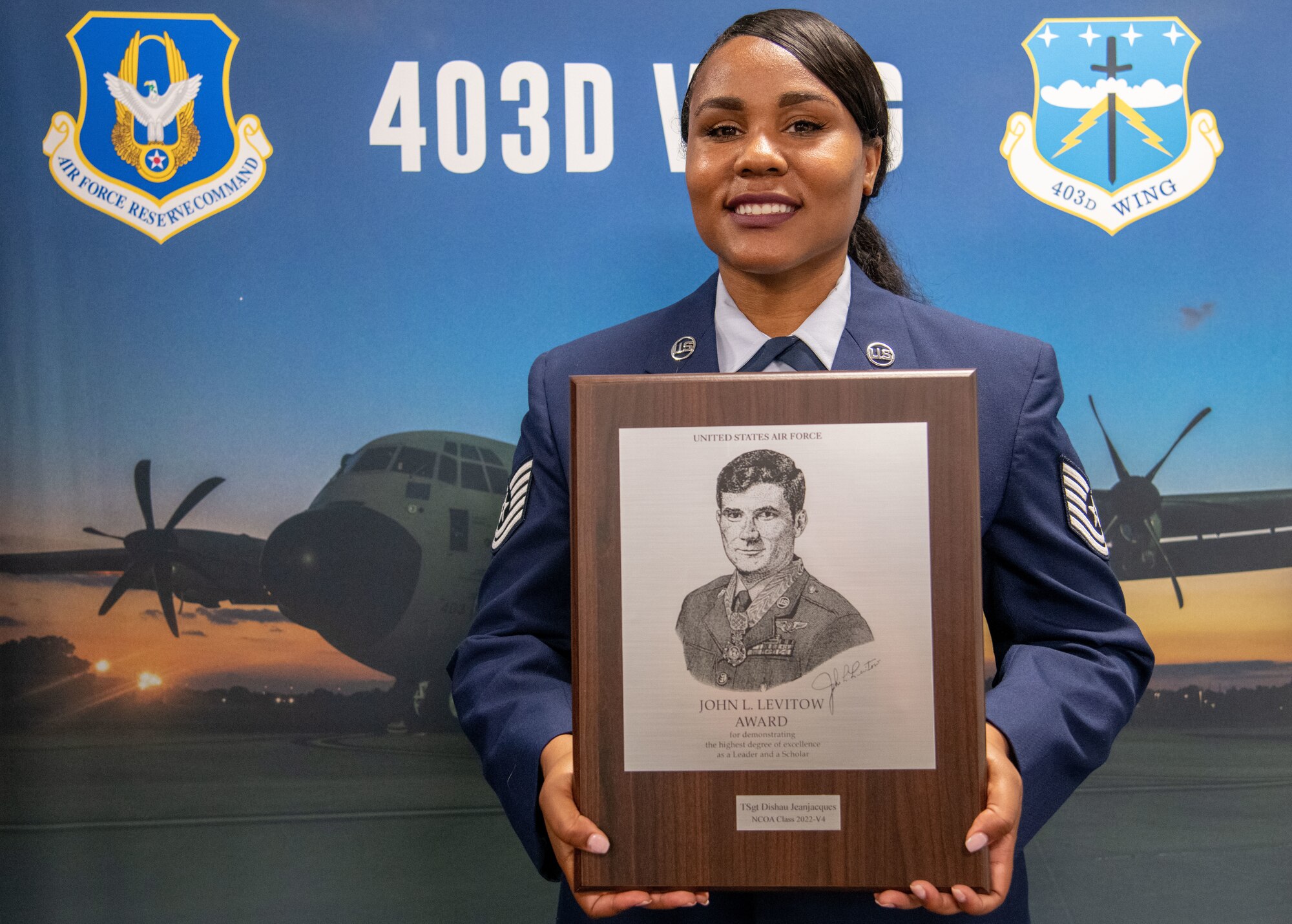 TSgt. JeanJacques stands in front of a 403d Wing display holding a plaque