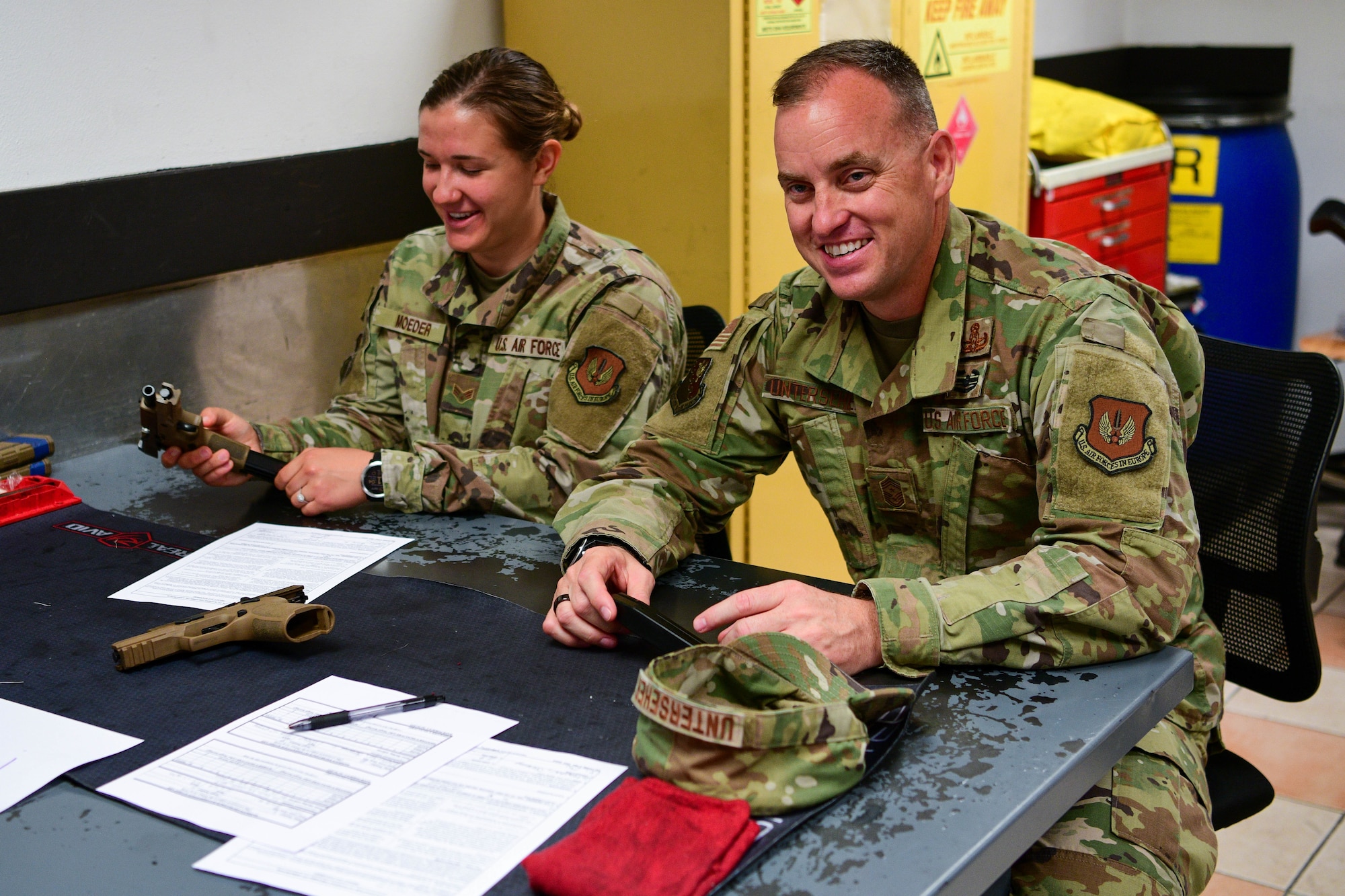U.S. Air Force Chief Master Sgt. Jeremy Unterseher, 31st Fighter Wing command chief, right, and U.S. Air Force Senior Airman Brooke Moeder, left, 31st FW public affairs specialist, attend a familiarization briefing during the 2022 Excellence in Competition Pistol match at Aviano Air Base, Italy, May 17, 2022. Combat arms instructors briefed participants on gun safety fundamentals and how to handle an M18 Handgun for the competition held in honor of Police Week. Police Week has been held annually since 1962, after President Kennedy designated the week of May 15 in remembrance of officers who have died in the line of duty. (U.S. Air Force photo by Airman 1st Class Calopedis)