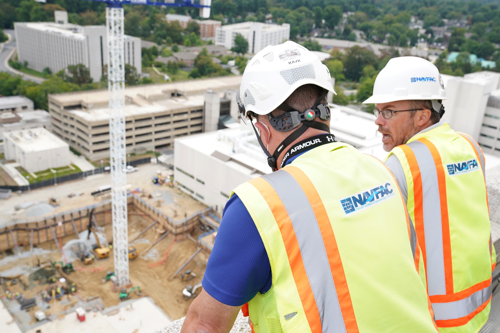 Two men wearing hard hats look down on a construction site.