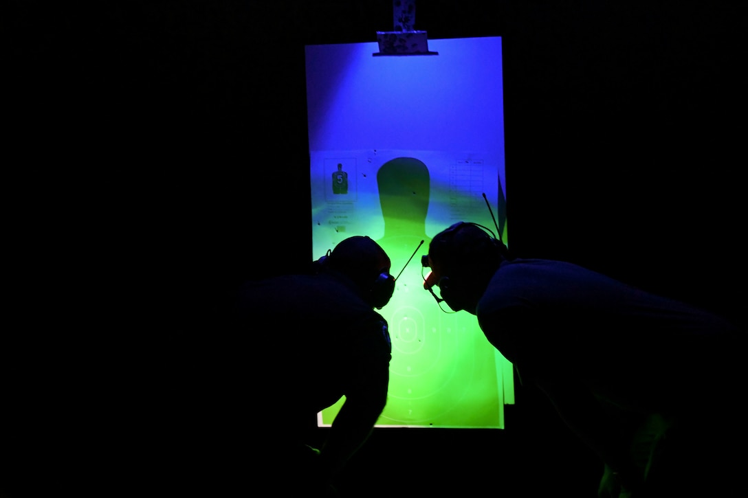 An airman and a civilian in a dark room look at an illuminated target.