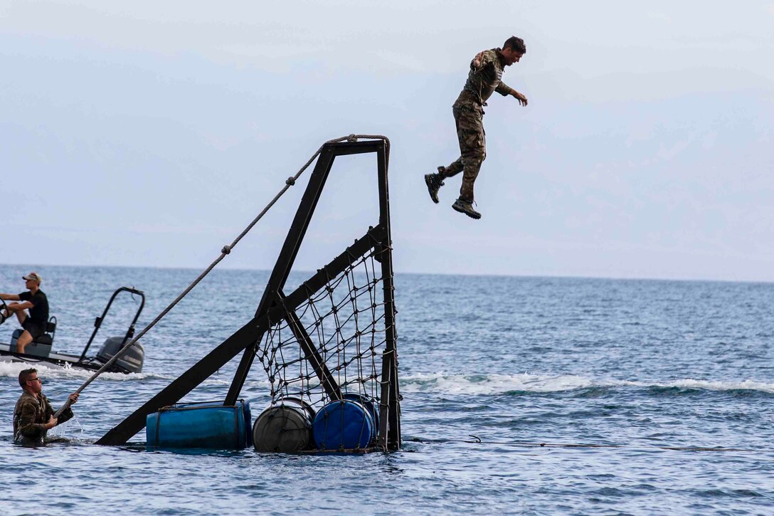 A service member jumps from an obstacle into a body of water.