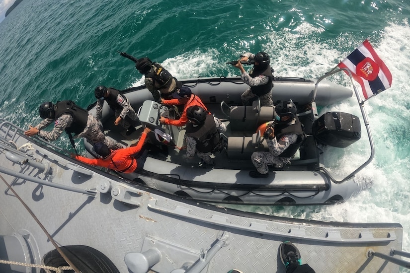 A small boat full of military personnel pulls up alongside a larger vessel.