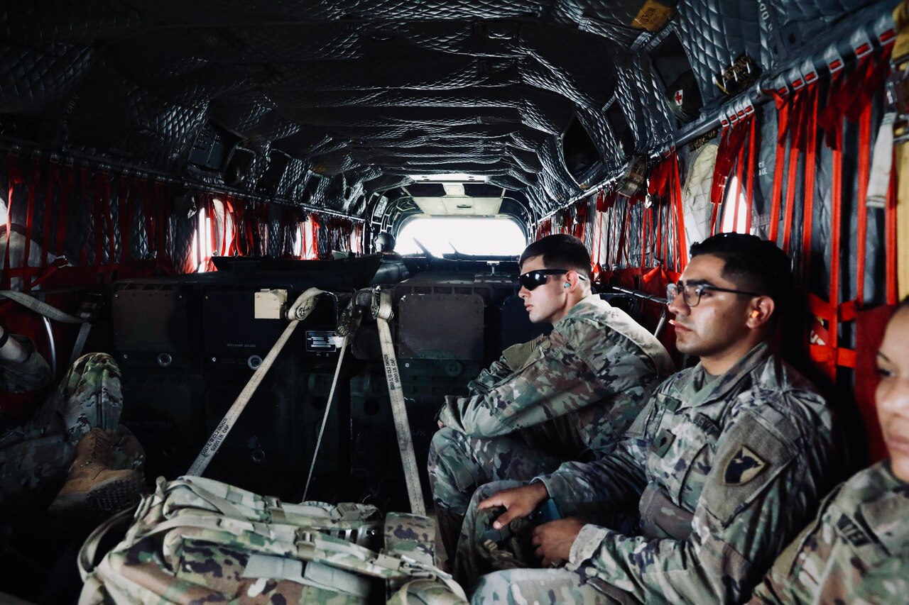 Soldiers sit in web seating in the rear of a helicopter.