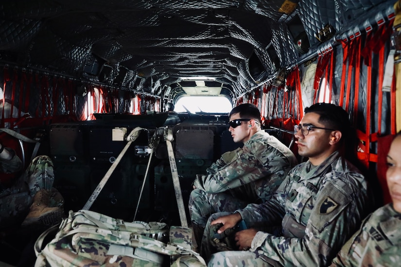 Soldiers sit in web seating in the rear of a helicopter.