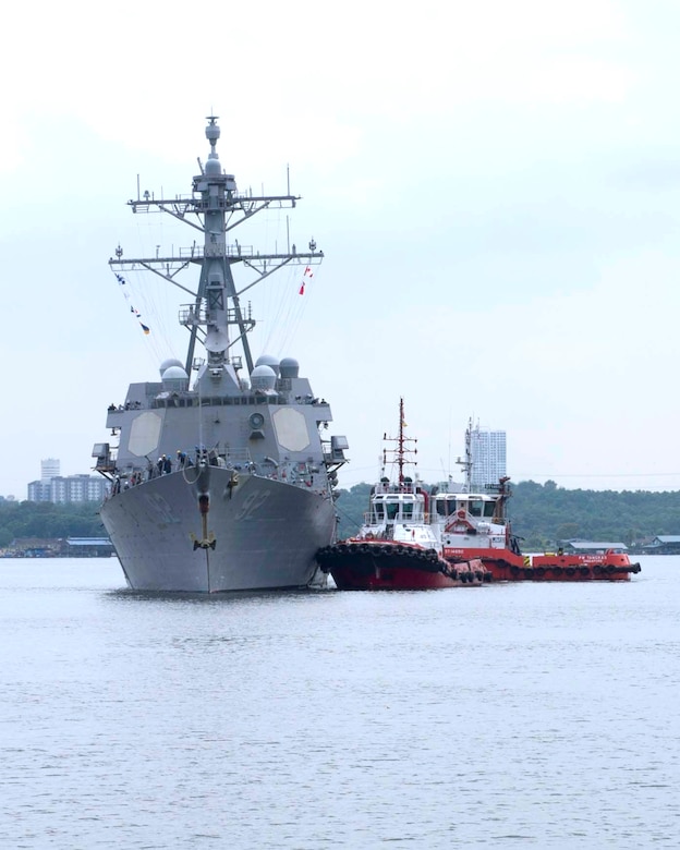 Two small watercraft pull up alongside a much larger military ship.