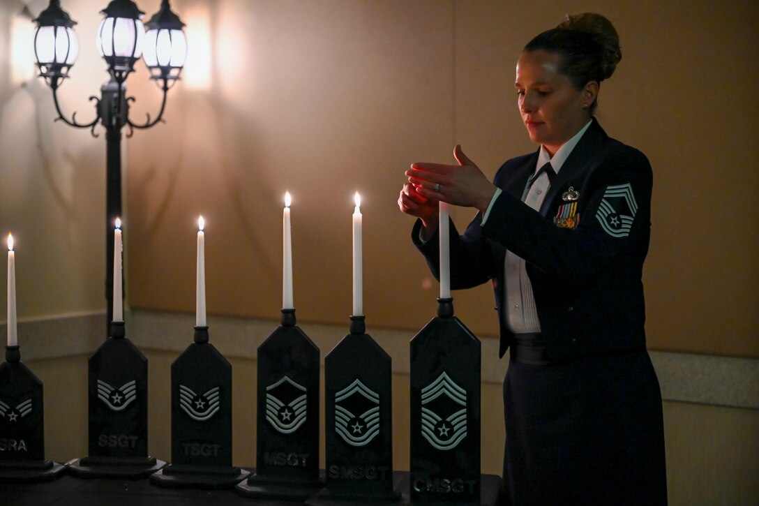 An airman lights a candle in a display of several lighted candles.