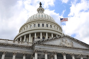 An up-angle view of a large building with a dome on top and an American flag flying.