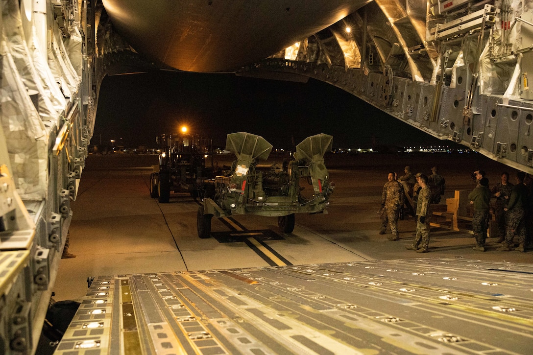 A large piece of equipment is moved toward the loading ramp of a military aircraft.