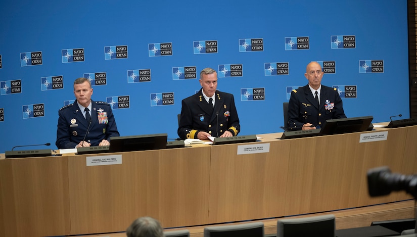 Many uniformed personnel are seated around a large circular desk.