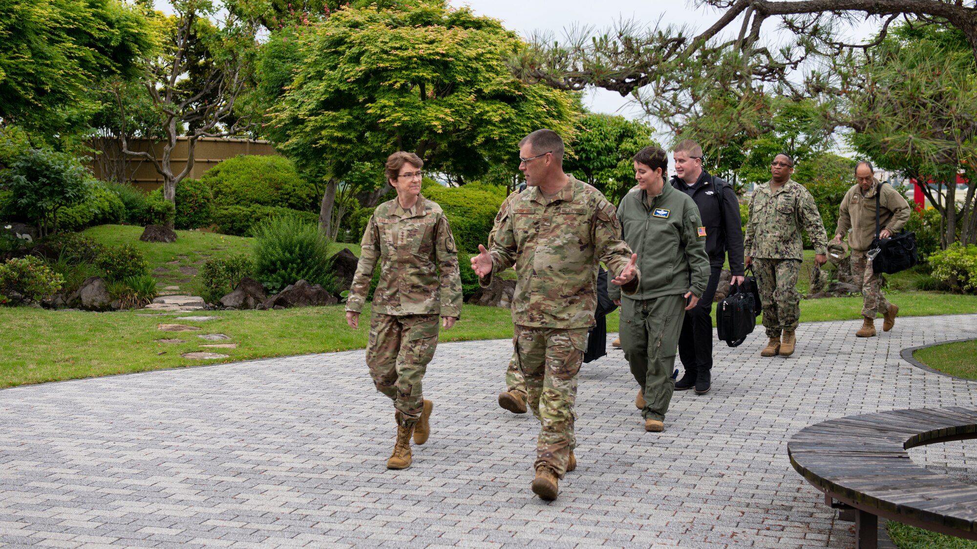 A female general and several other officers walk through a Japanese garden