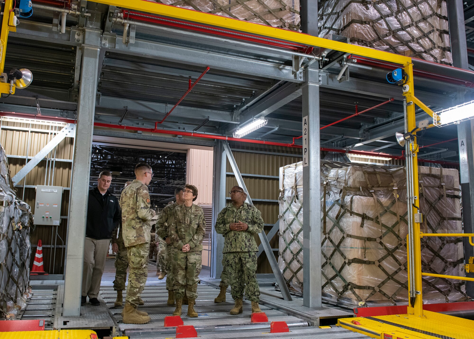 A female general standing in a large entry way to a large air freight storage area