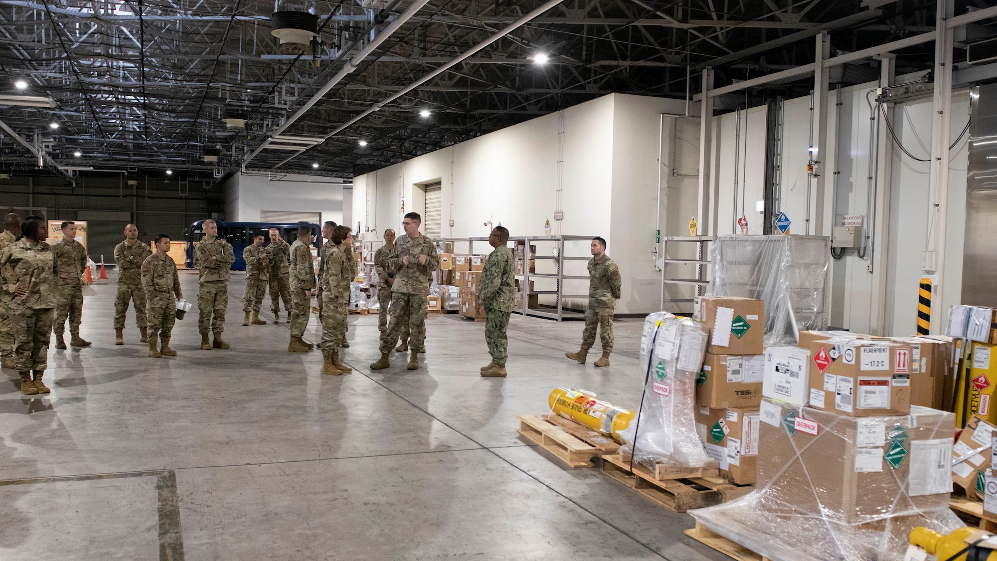 A far away view of a female general being escorted through a military warehouse