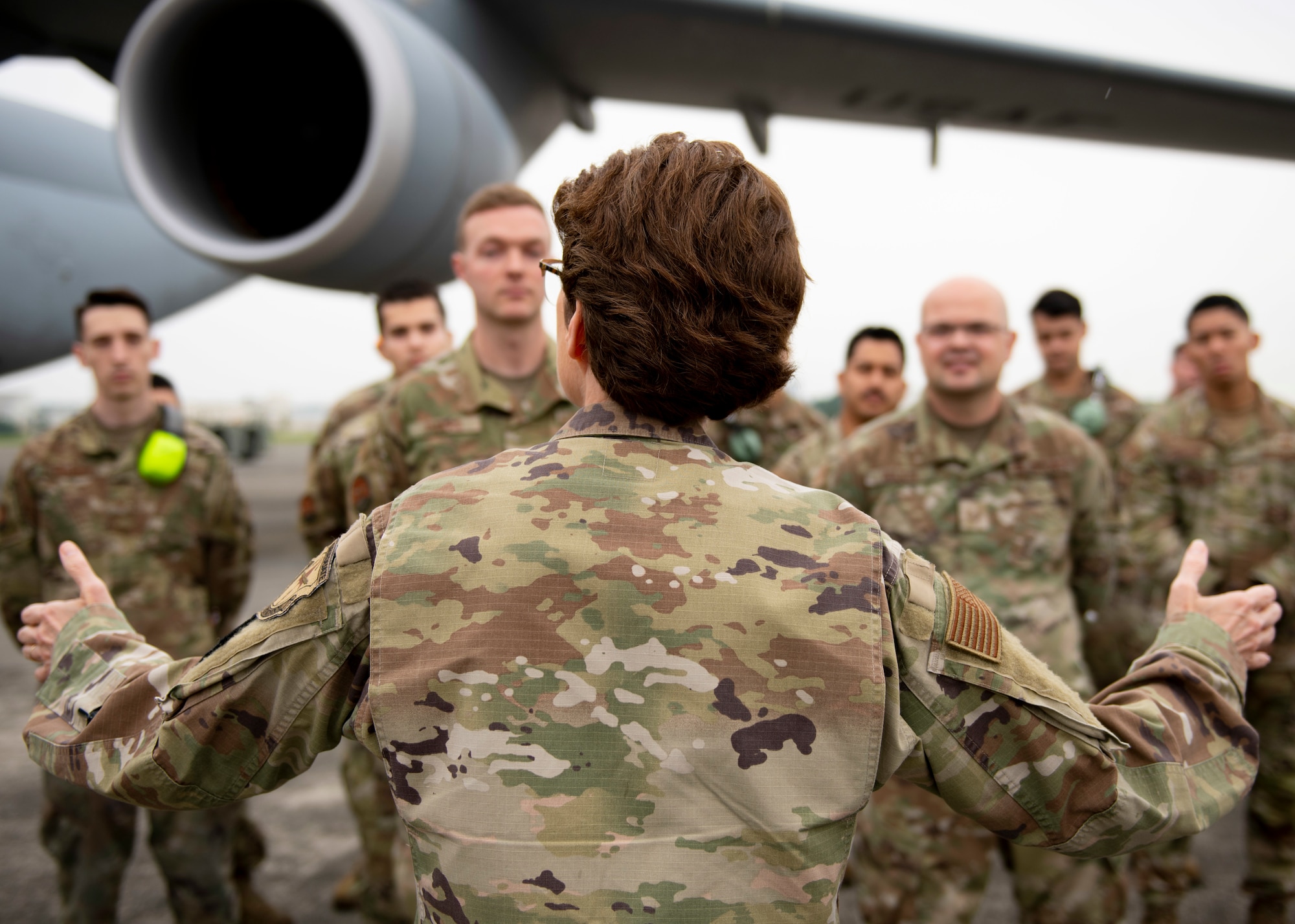 A view from behind a female general speaking to assembled troops in formation, facing her