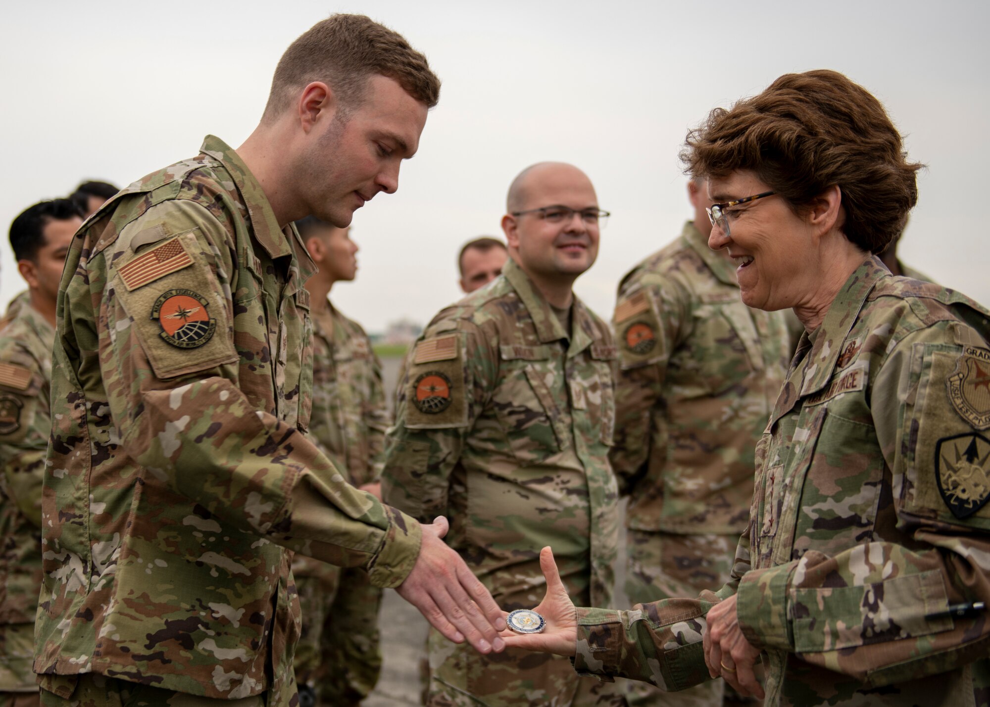 A female general hands a coin to a sergeant on a flight line