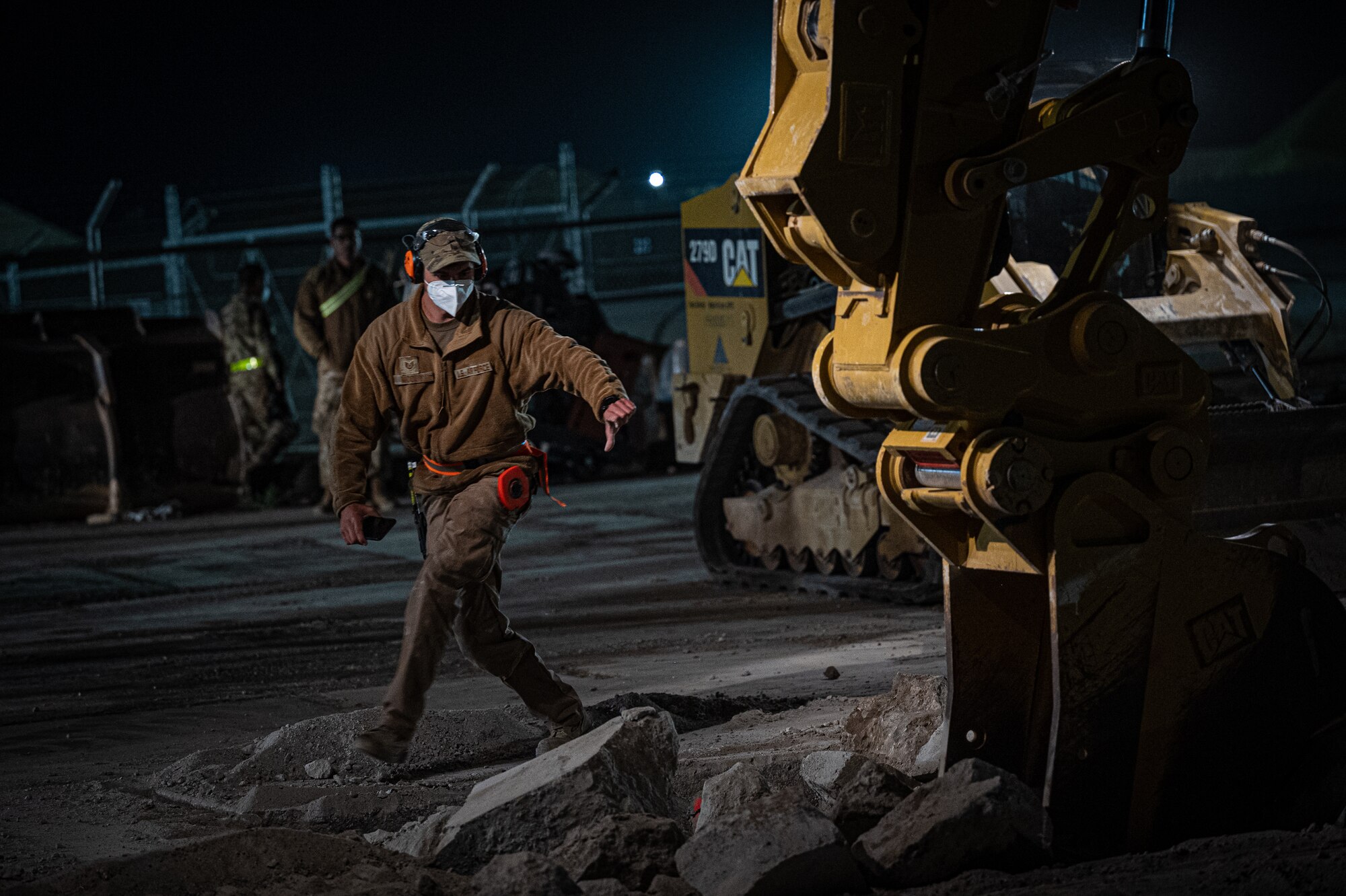 Technical Sgt. David McCoy, 332d Expeditionary Civil Engineer Squadron non-commissioned officer in charge of airfield pavements and logistics, gives spotting instructions to an excavator operator to remove debris and prepare a crater for backfill material during a rapid airfield damage recovery exercise at an undisclosed location in Southwest Asia, May 12, 2022. RADR exercises test the ability of the 332d ECES to rapidly repair runways and runway support structures to recover and resume airfield operations after it has experienced significant damage. (U.S. Air Force photo by Master Sgt. Christopher Parr)