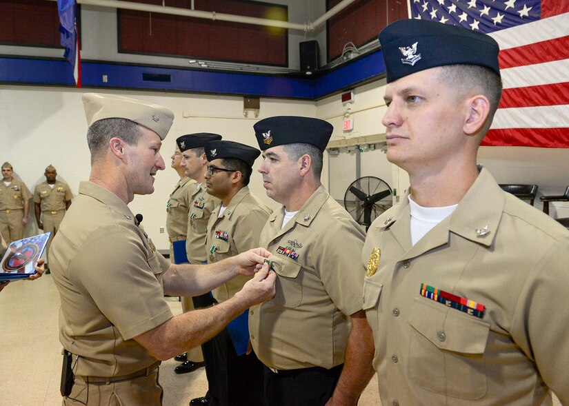 A sailor places a medal on the uniform of another sailors as others stand on either side.