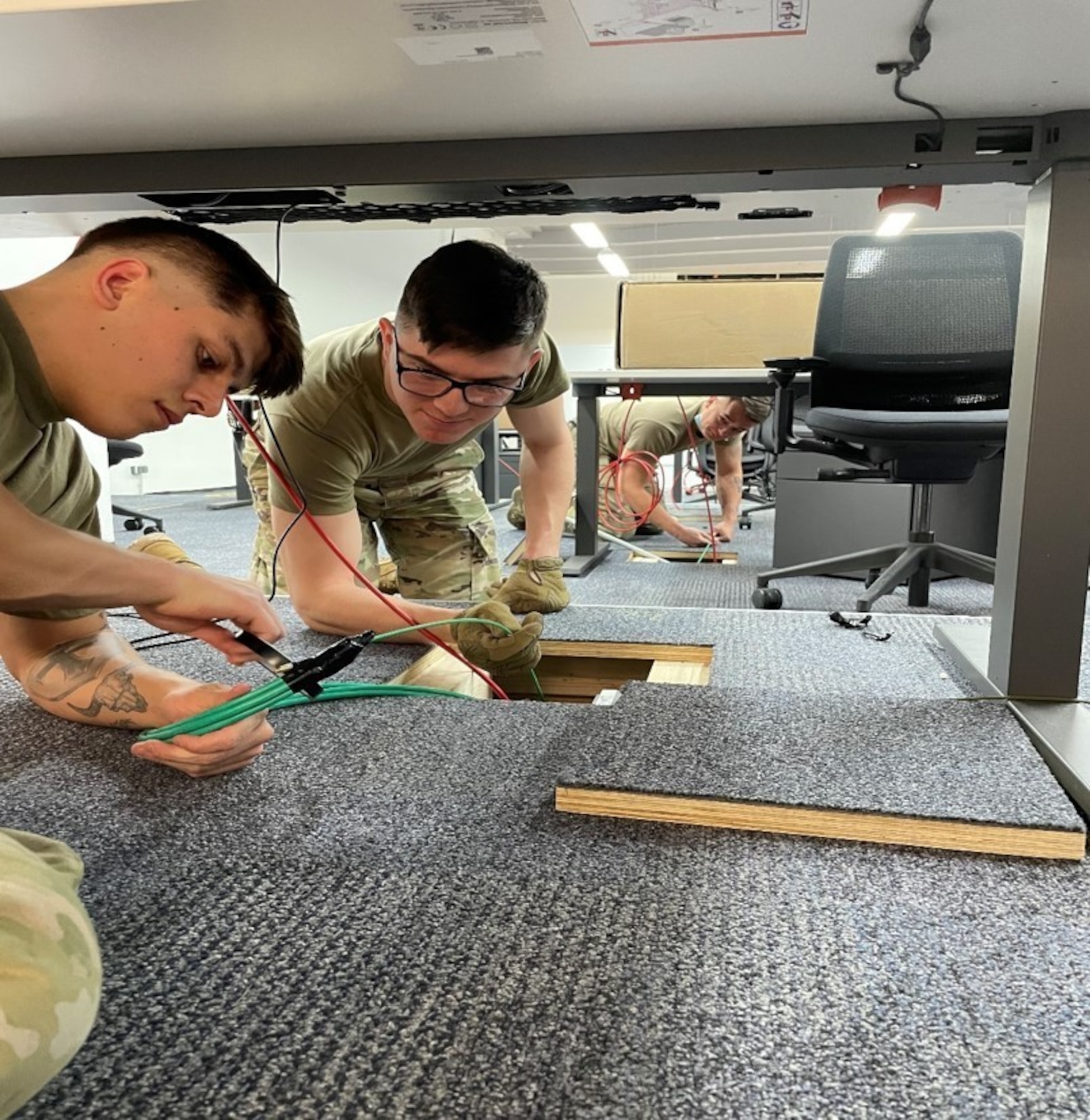 Three Airmen installing network cables in an office.