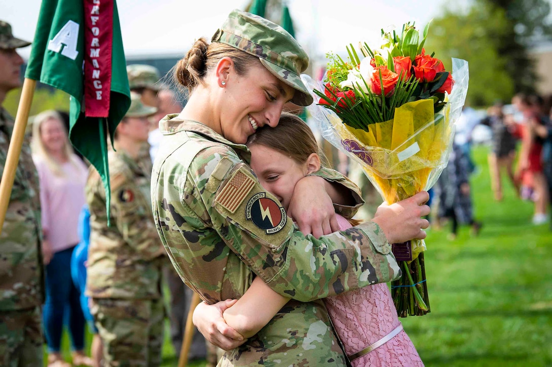 A cadet candidate  hugs a young girl while holding flowers.