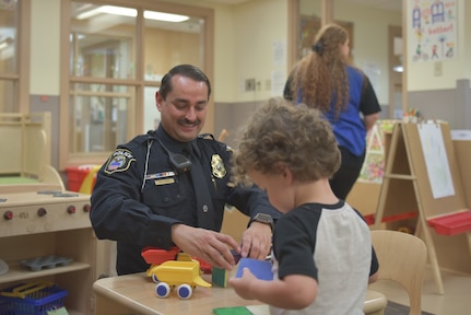 Man in police uniform plays with a child at a child development center.