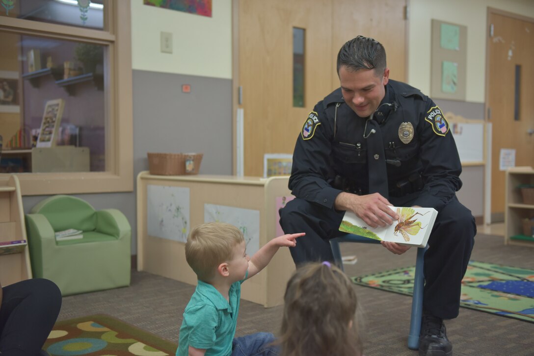 Man in police uniform reads stories to children at a child development center.