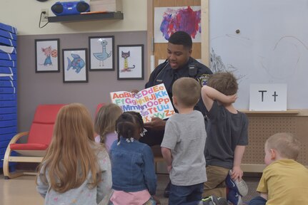 Man in police uniform reads stories to children at a child development center.