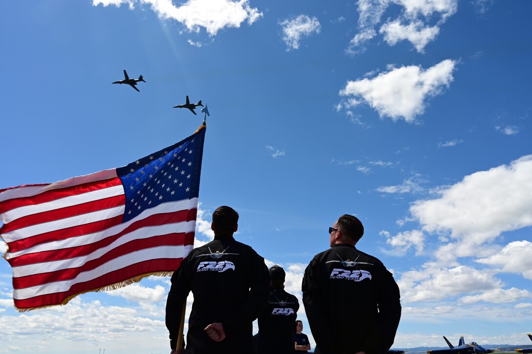 Two B-1B Lancers fly over members of the U.S. Air Force F-22 Raptor Demonstration Team at the 2022 Ellsworth Air and Space Show at Ellsworth Air Force Base, S.D., May 15, 2022. The team conducted an enlistment ceremony for four future Airmen on the flightline during the air show. (U.S. Air Force photo by Staff Sgt. Hannah Malone)