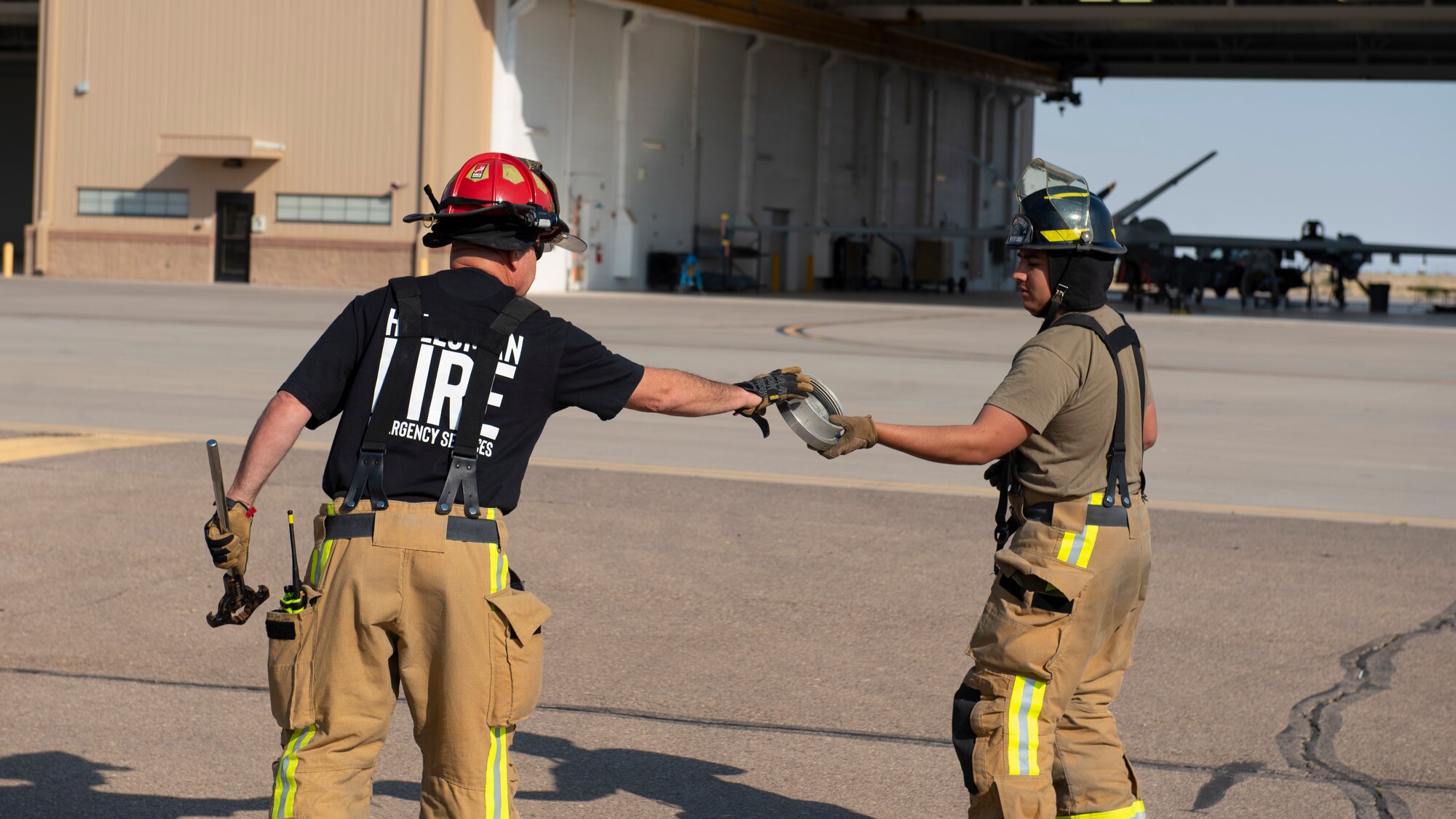 Airman 1st Class Kevin Gomez (right), 49th Civil Engineer Squadron firefighter hands Norman Bloom (left), 49th CES company officer, a fire hose adapter during an emergency response training exercise, May 19, 2022, on Holloman Air Force Base, New Mexico.