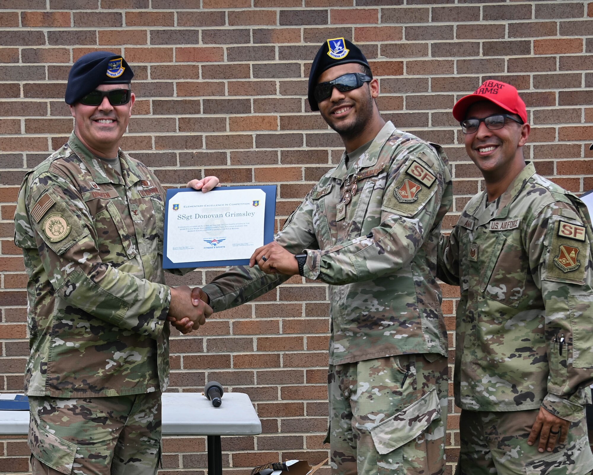 Staff Sgt. Donovan Grimsley, 316th Security Forces Squadron response force leader, center, is presented an Excellence in Competition badge by Col. Ian Dinesen, 316th Security Forces Group commander, near the Tactical Fitness Center at Joint Base Andrews, Md., May 20, 2022. Grimsley received the badge as an award for finishing in the top 10% of more than 300 shooters during a shooting competition. (U.S. Air Force photo by Airman 1st Class Isabelle Churchill