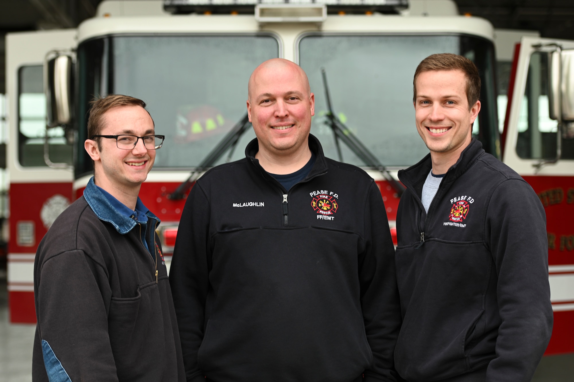 3 Firefighters stand in front of a firetruck.