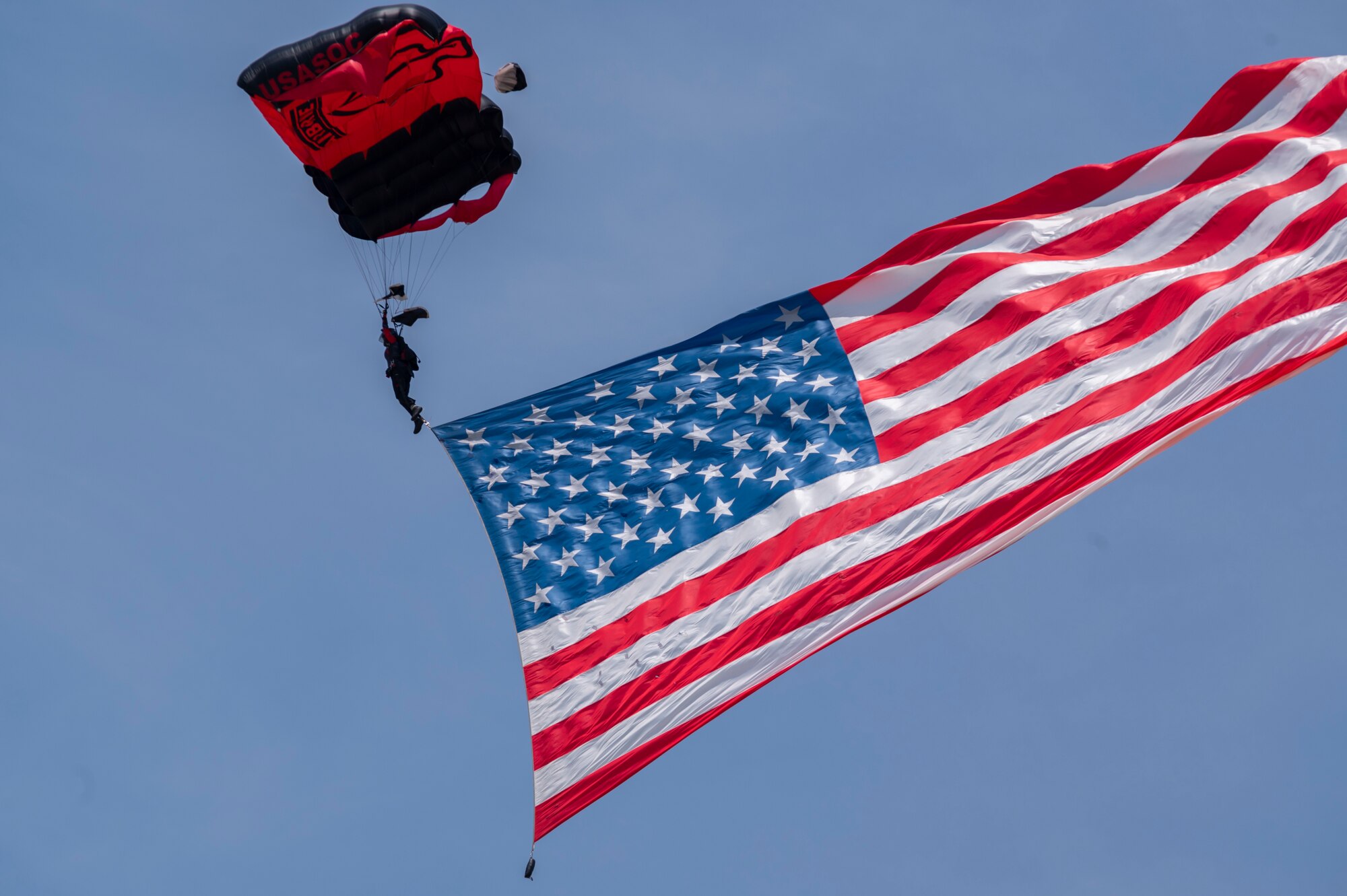 A member of the Black Daggers parachute team glides through the air with a U.S. Flag, May 21, 2022, during the first day of the 2022 Thunder Over Dover Airshow at Dover Air Force Base, Delaware. The Black Daggers are the U.S. Army Special Operations Command’s parachute demonstration team. (U.S. Air Force photo by Airman Simonne Barker)