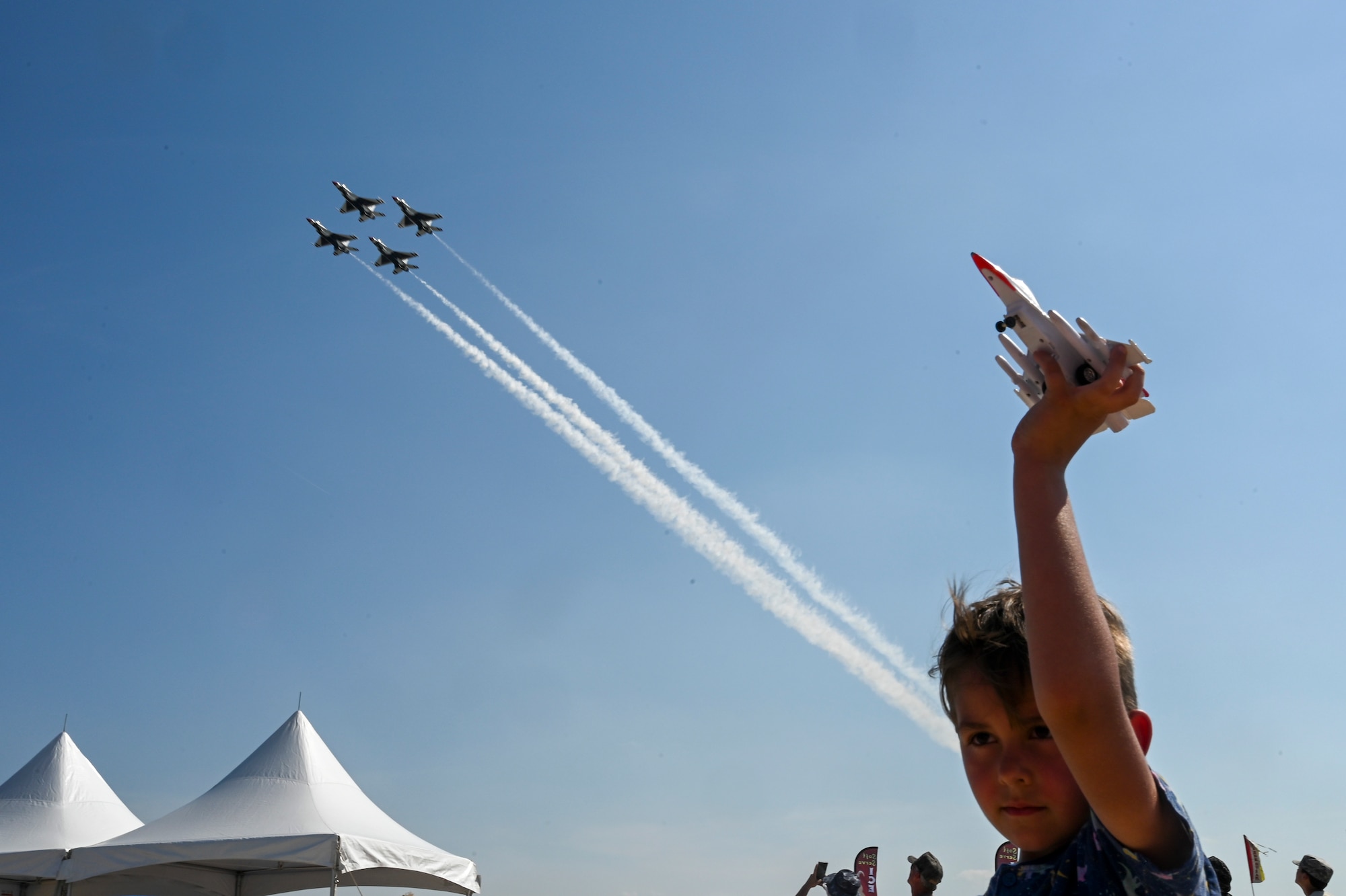 A child watches the U.S. Air Force Thunderbirds while playing with a Thunderbird toy during the first day of the 2022 Thunder Over Dover Airshow, May 21, 2022, at Dover Air Force Base, Delaware. The Thunderbirds performed precision flying maneuvers during the 2022 Thunder Over Dover Open House and Airshow May 21-22. (U.S. Air Force photo by Staff Sgt. Sabatino DiMascio)