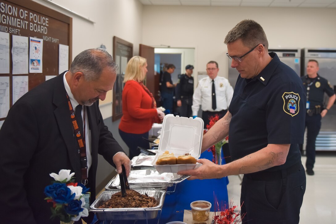 A woan in red and a man in a suit serve food to Police officers.