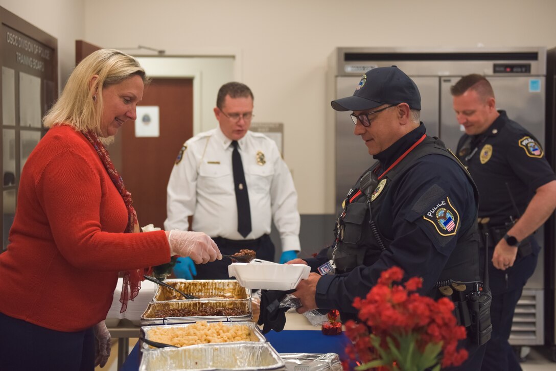 A woman dressed in red serves food to a police officer.