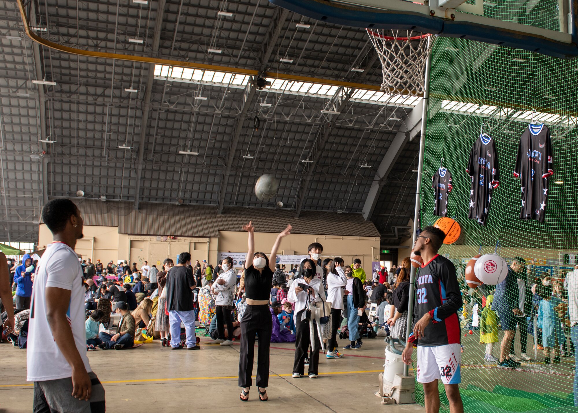 A masked woman tosses a basketball at a hoop at a festival booth