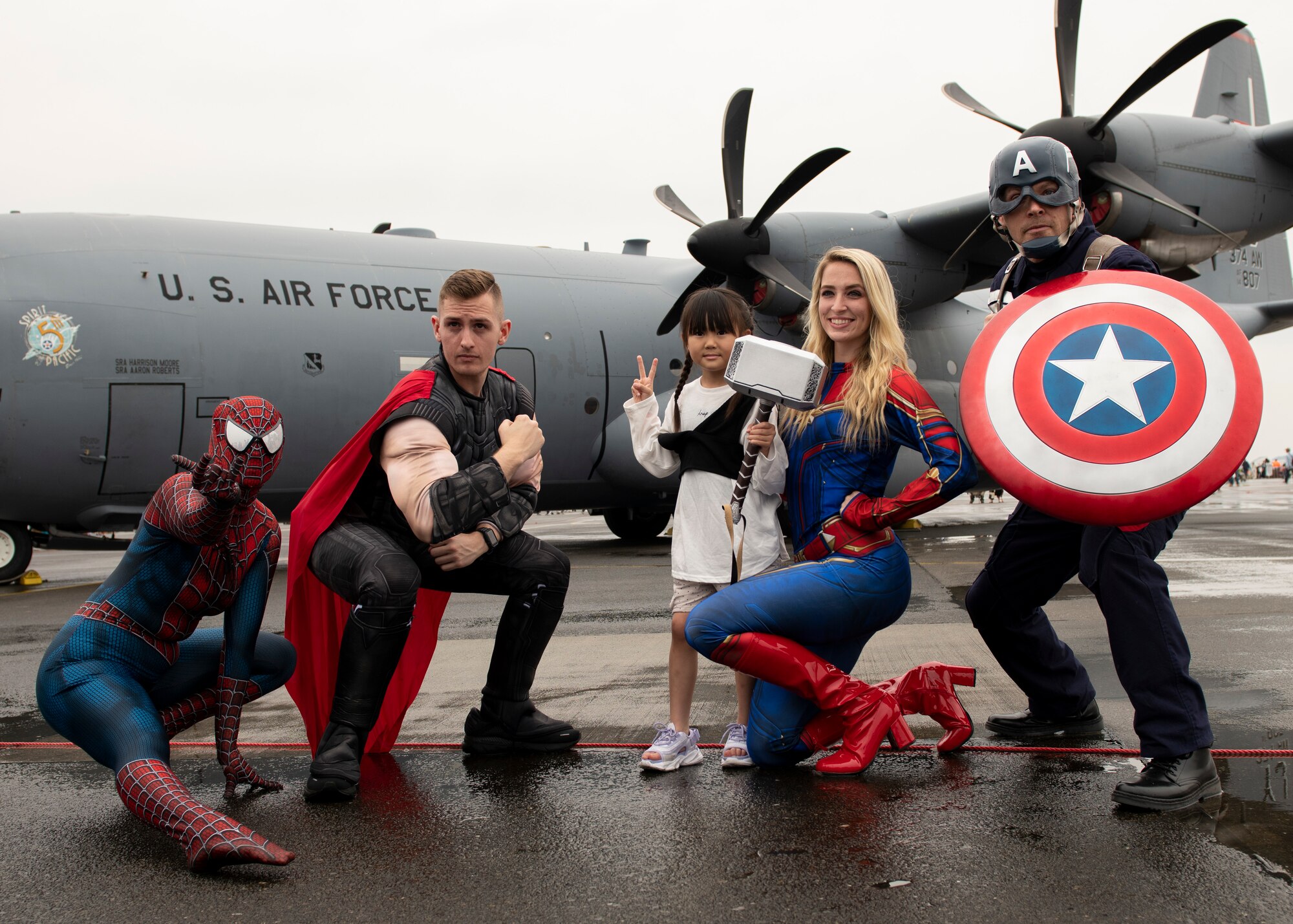 A young girl poses for a picture with Spiderman, Thor, Captain Marvel, and Captain America
