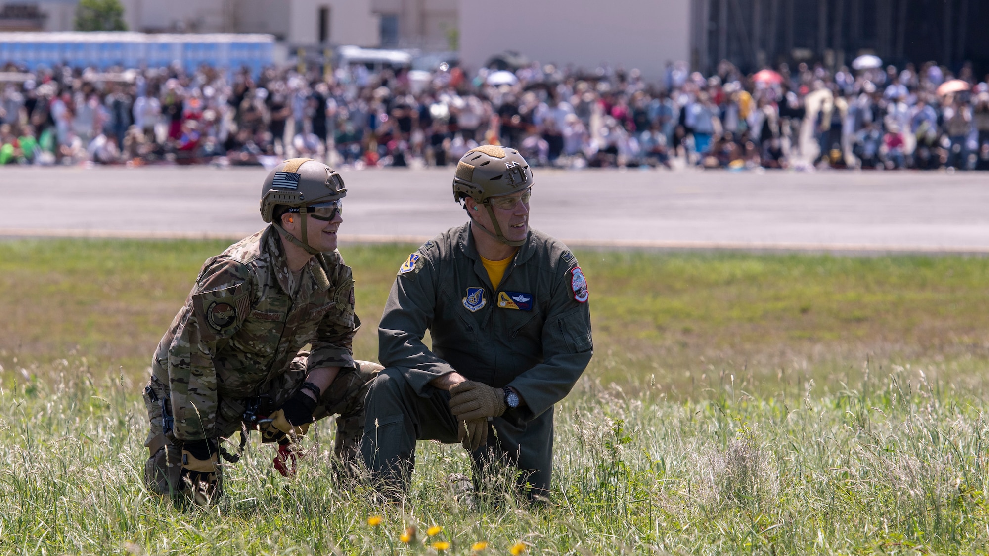 Two Airmen wait on a grassy knoll in front of a crowd