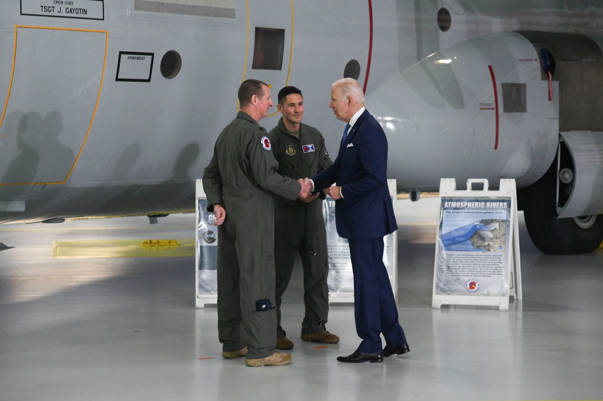 President Biden shakes Lt. Col. Olson's hand as Dehart looks on. A WC-130J aircraft is in the background