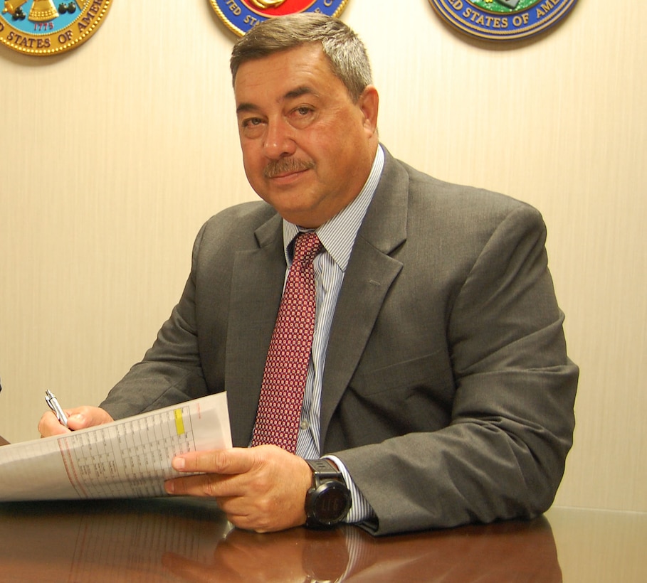 Man seats at a table wearing a gray suit and red tie with a blue dress shirt