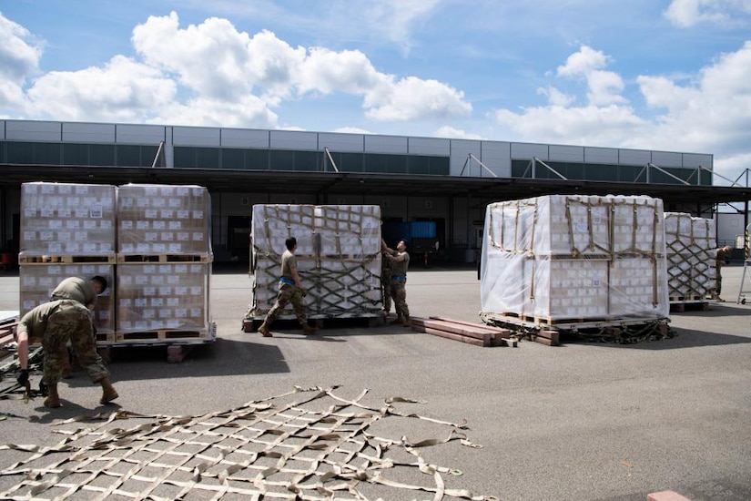 Several uniformed service members place infant formula onto wooden pallets.