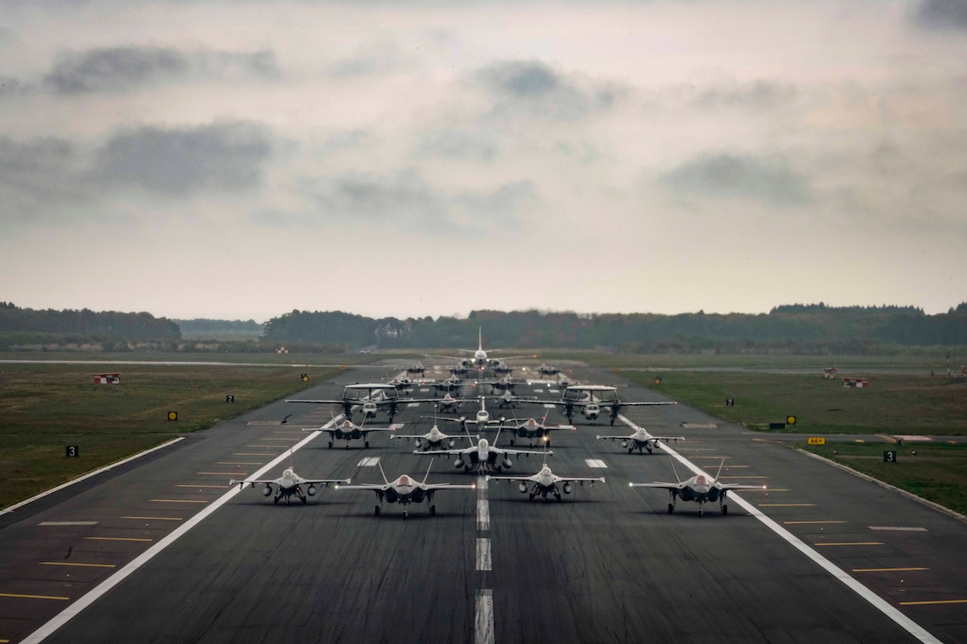 U.S. Air Force and Navy and Japanese air force aircraft sit in formation on a tarmac.