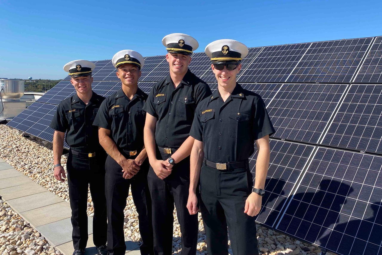 Four uniformed students at the U.S. Naval Academy stand outside near a solar panel service.
