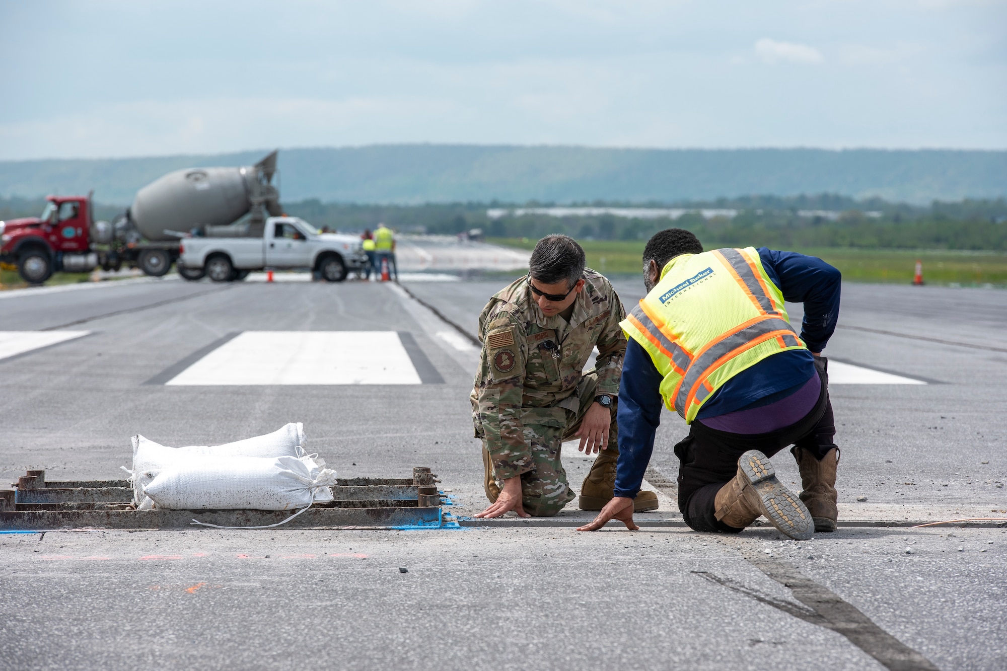 U.S. Air Force Senior Master Sgt. Alan Romero, 167th Airlift Wing airfield manager, and a contractor with engineering firm Michael Baker International, look at a trench dug in the runway at Shepherd Field as part of an airfield lighting upgrade project, May 5, 2022. Lighting on the runway and the military and civilian sides of the airfield are being upgraded as part of a military construction cooperative agreement.