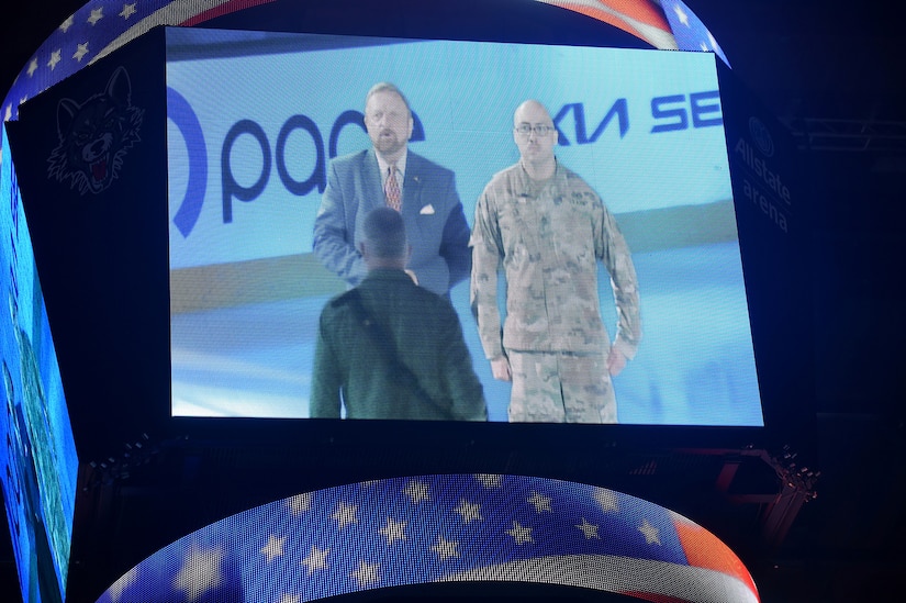 Wayne Messmer, left, Senior Executive Vice President, Chicago Wolves, and Sgt. 1st Class Moises Garcia appear on the Jumbotron before the singing of the National Anthem during a Chicago Wolves military appreciation game, May 21, 2022, at the All-State Arena.