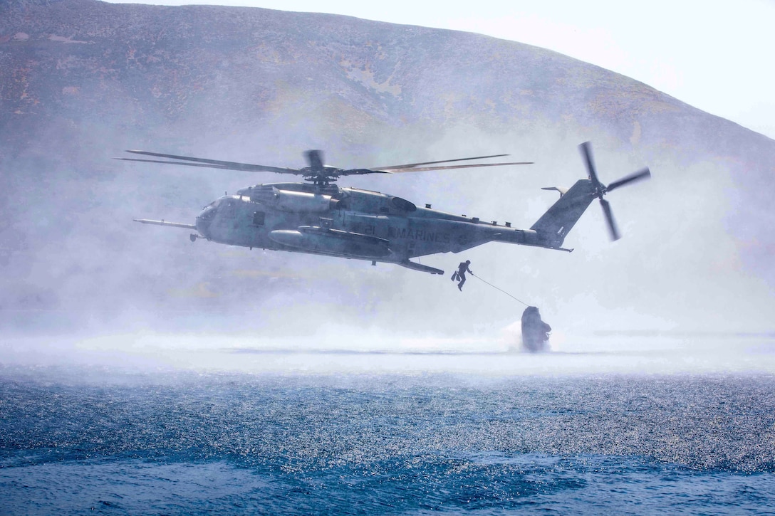 A Marine exits an airborne helicopter toward an inflatable boat.
